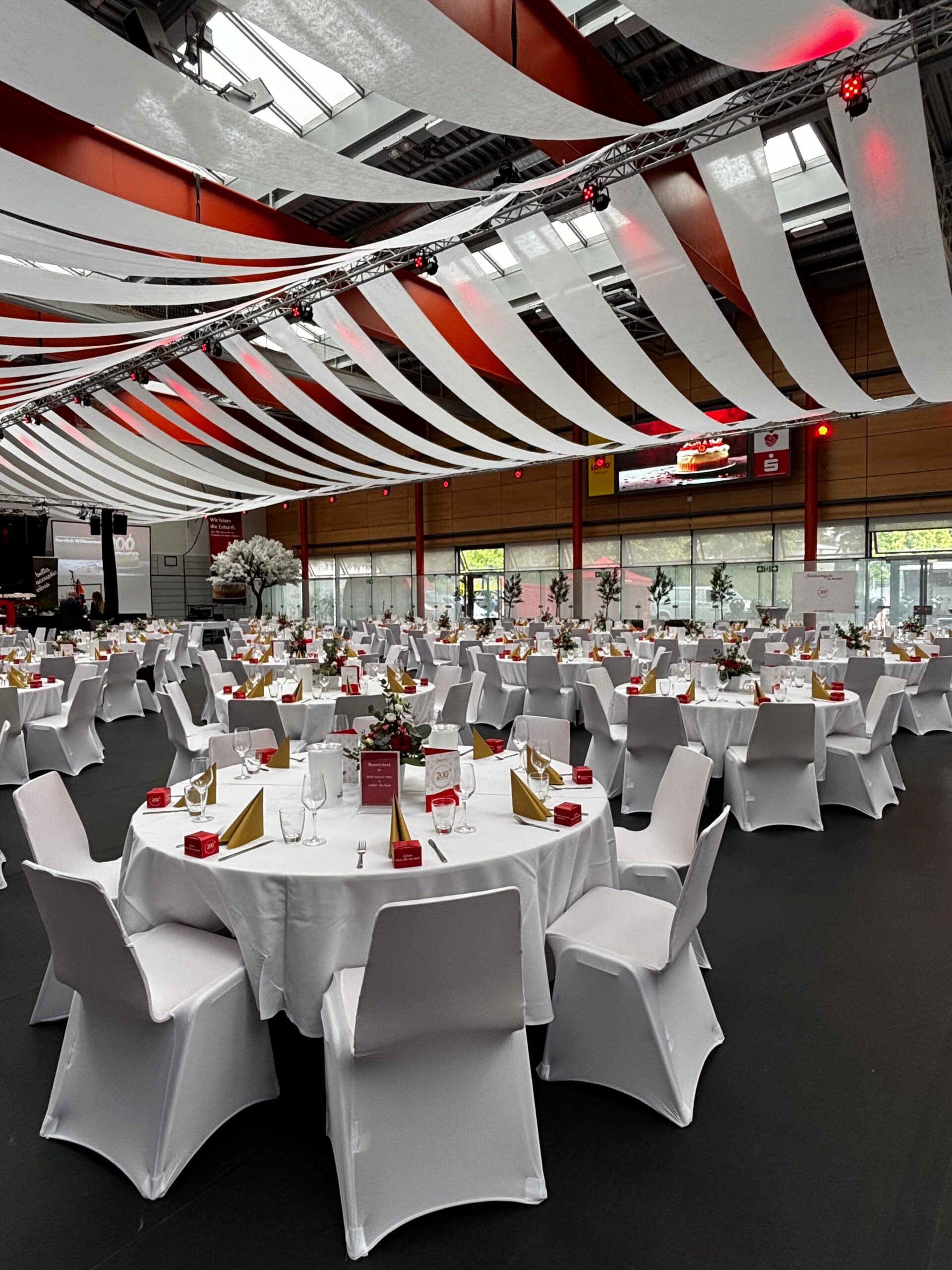 Festsaal mit rot-weißer Deckenabhängung und runden Tafeln