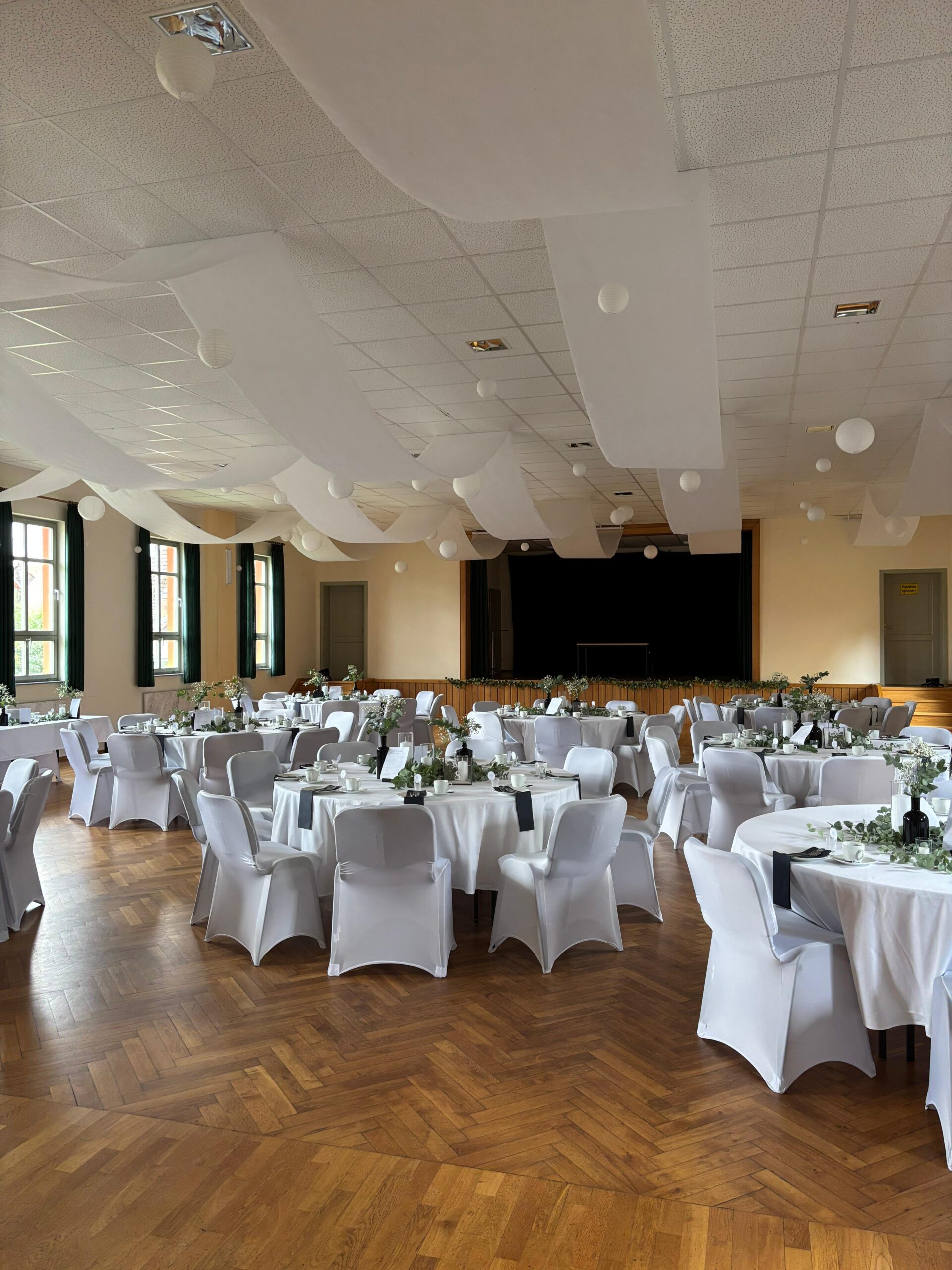 Heller Festsaal mit runden Tafeln und Stuhlhussen