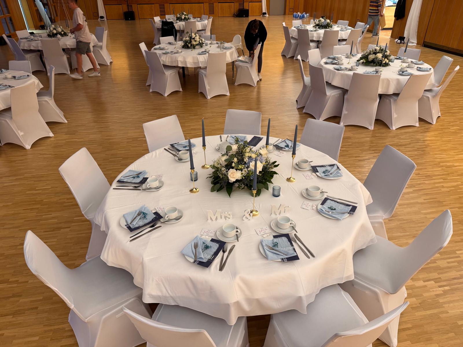 Gedeckter runder Hochzeitstisch mit Blumen und Stuhlhussen