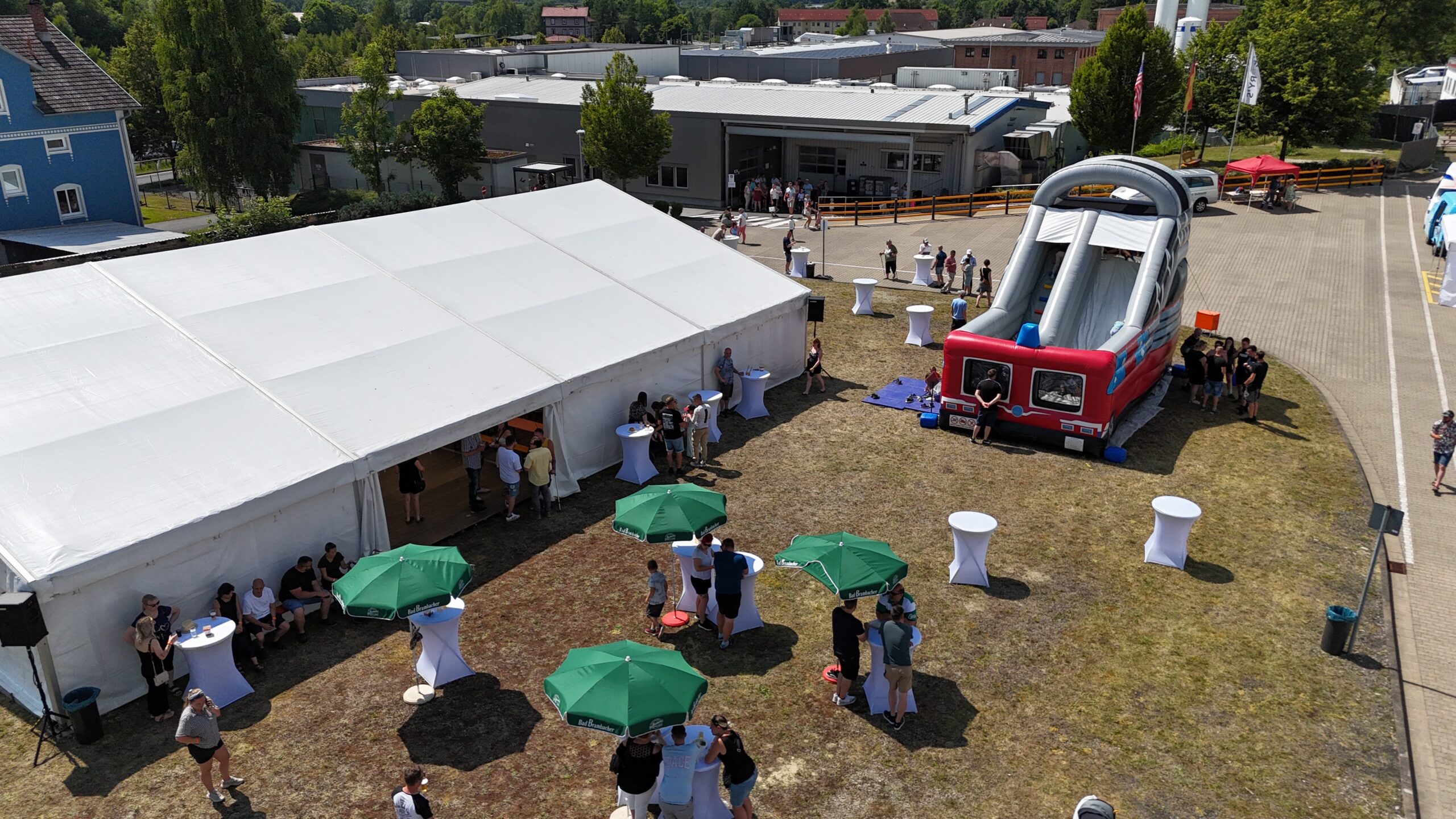 Sommerfest mit Zelt, Hüpfburg und Gästen auf einem Firmengelände von oben