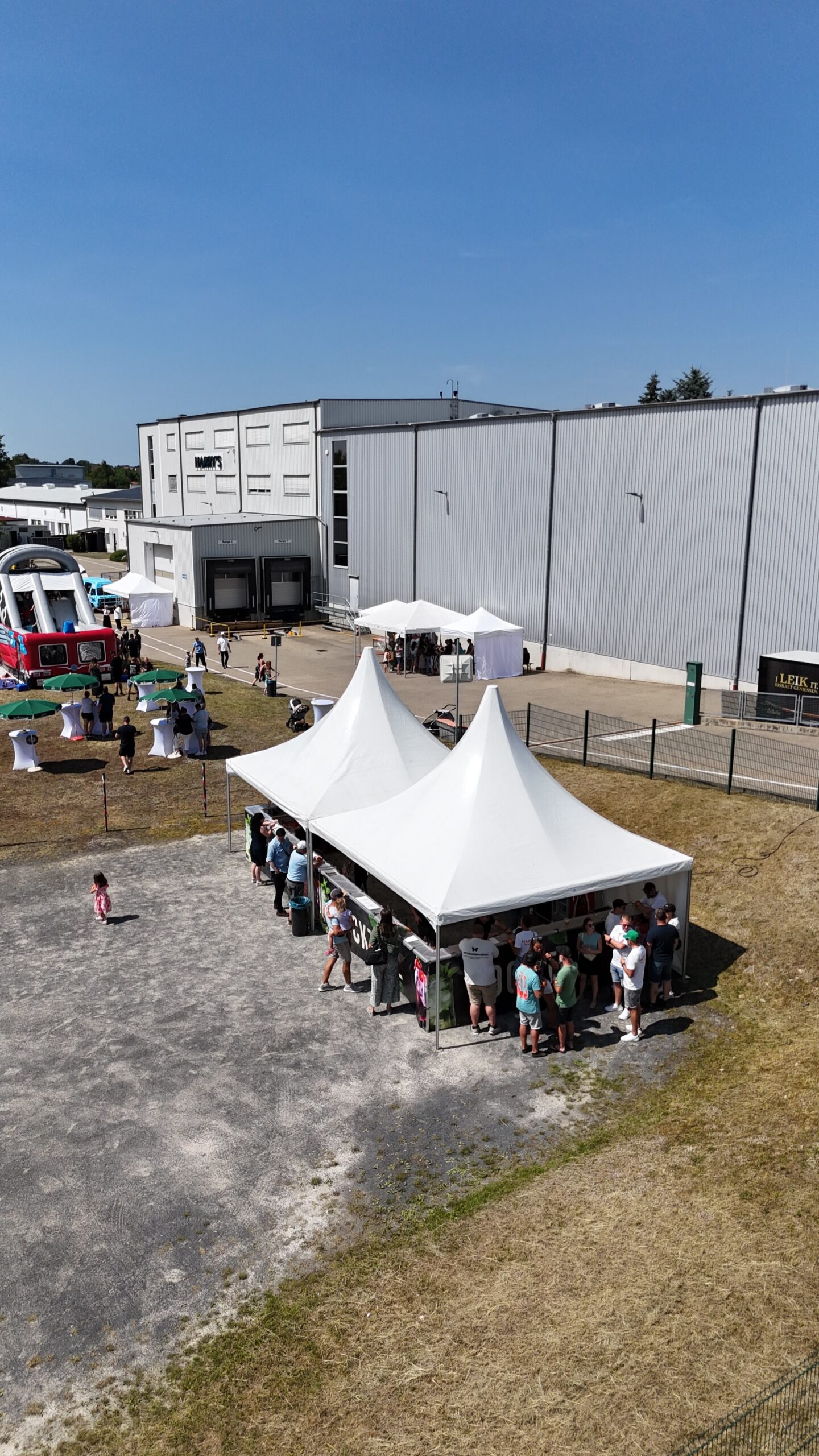 Luftaufnahme: Sommerfest mit Pagodenzelten vor einer Firmenhalle