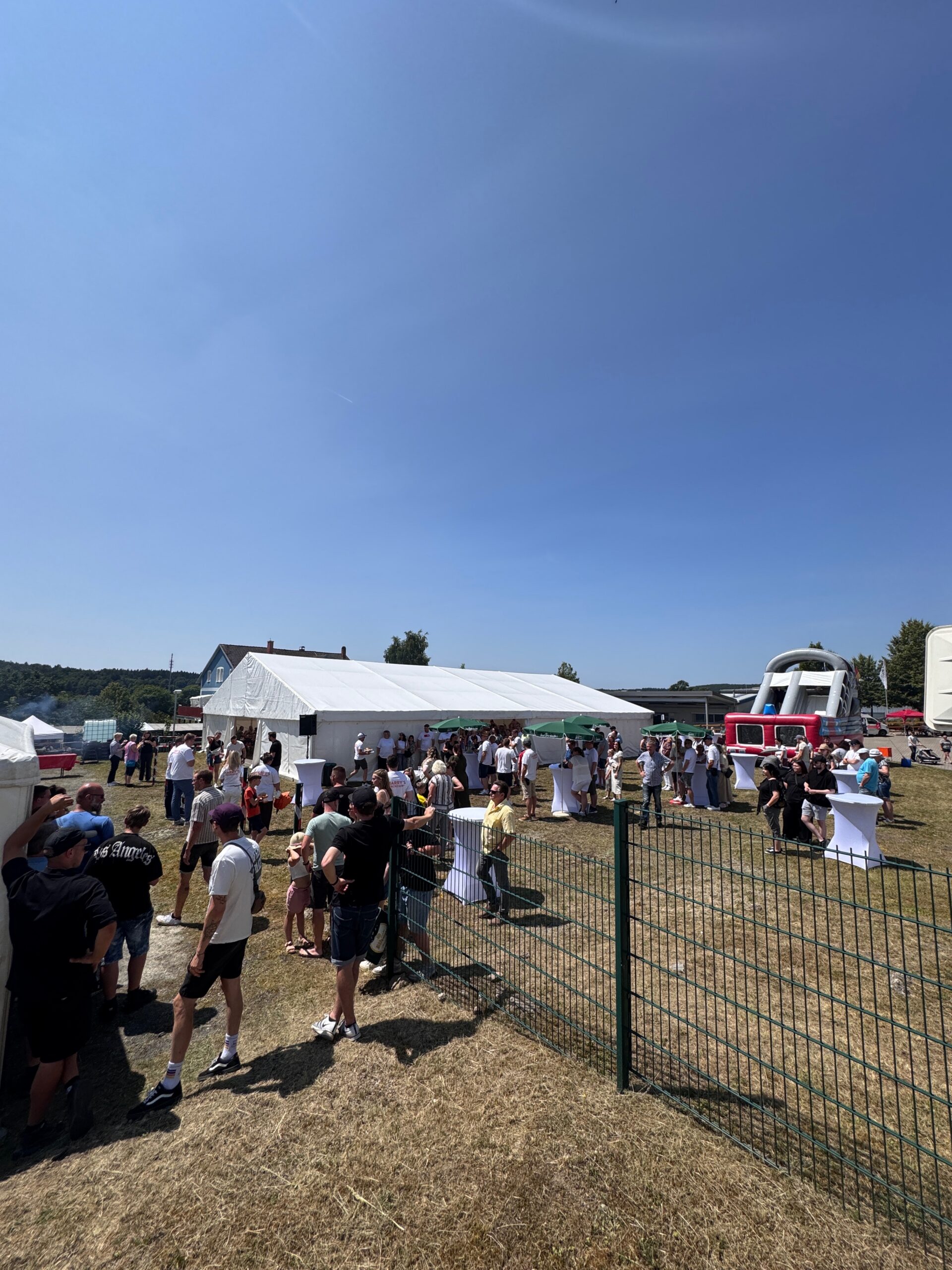 Fest auf einer Wiese mit Zelt, Hüpfburg und vielen Gästen