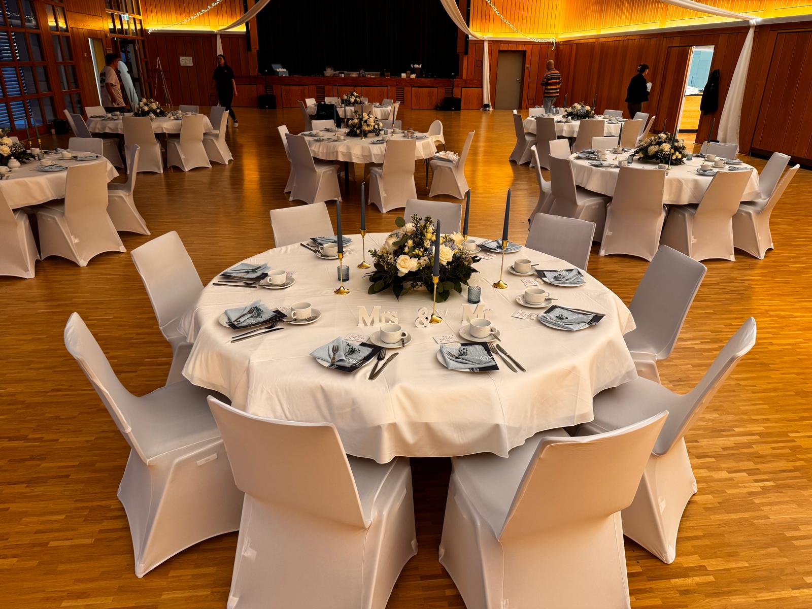 Festsaal mit gedeckten runden Tafeln und Stuhlhussen