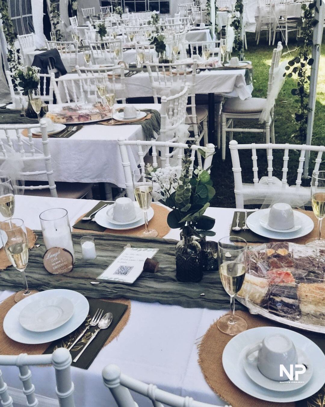 Gedeckte Tafel mit weißen Stühlen auf dem Rasen unter dem Zelt