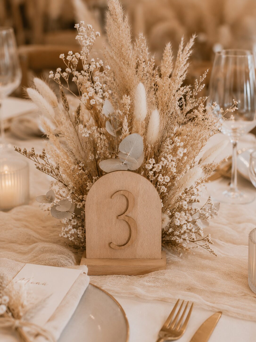 Tischnummer aus Holz zwischen Trockenblumen auf einem Hochzeitstisch