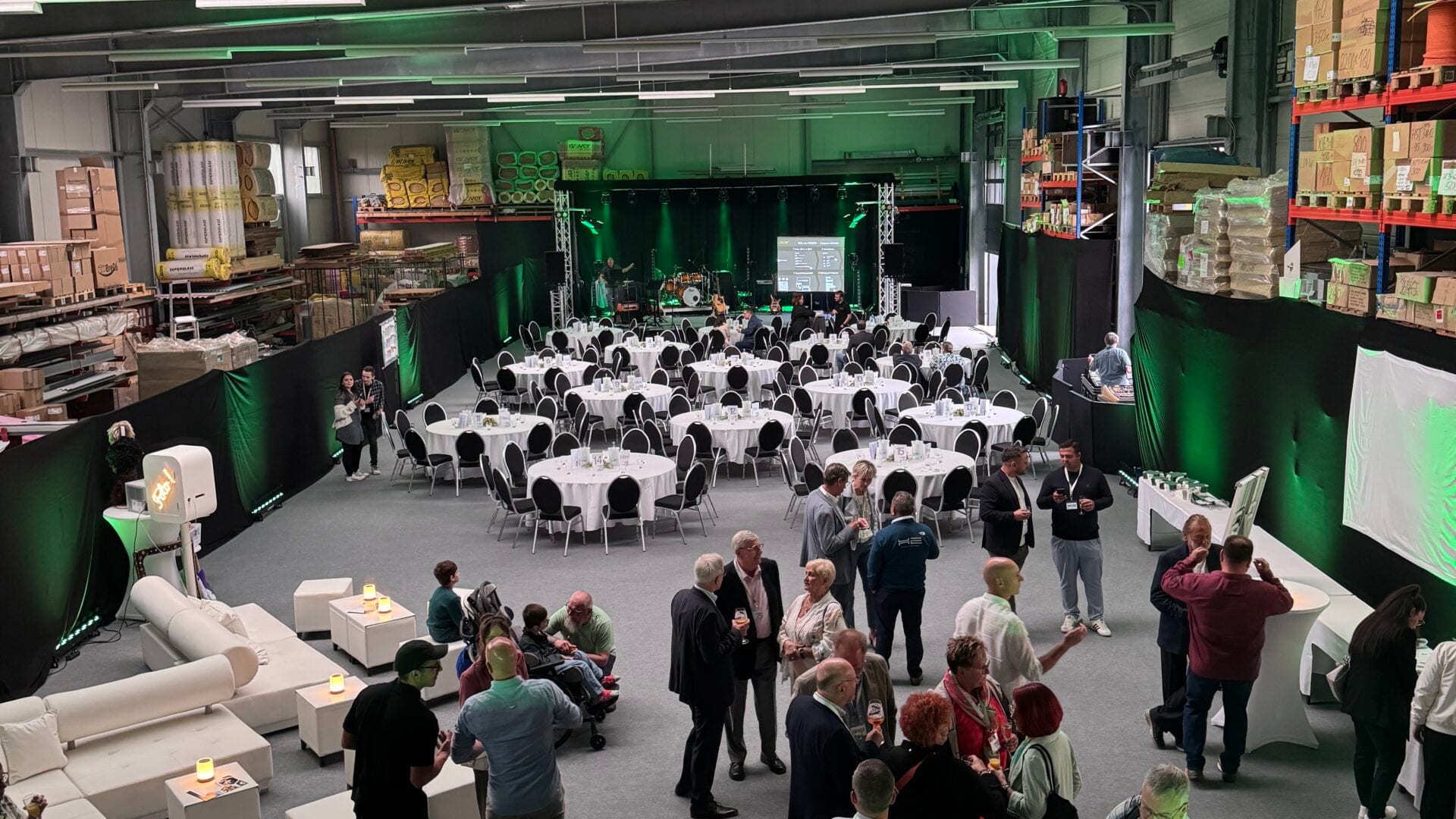 Firmenjubiläum in einer Halle mit Gästen, runden Tafeln und Bühne